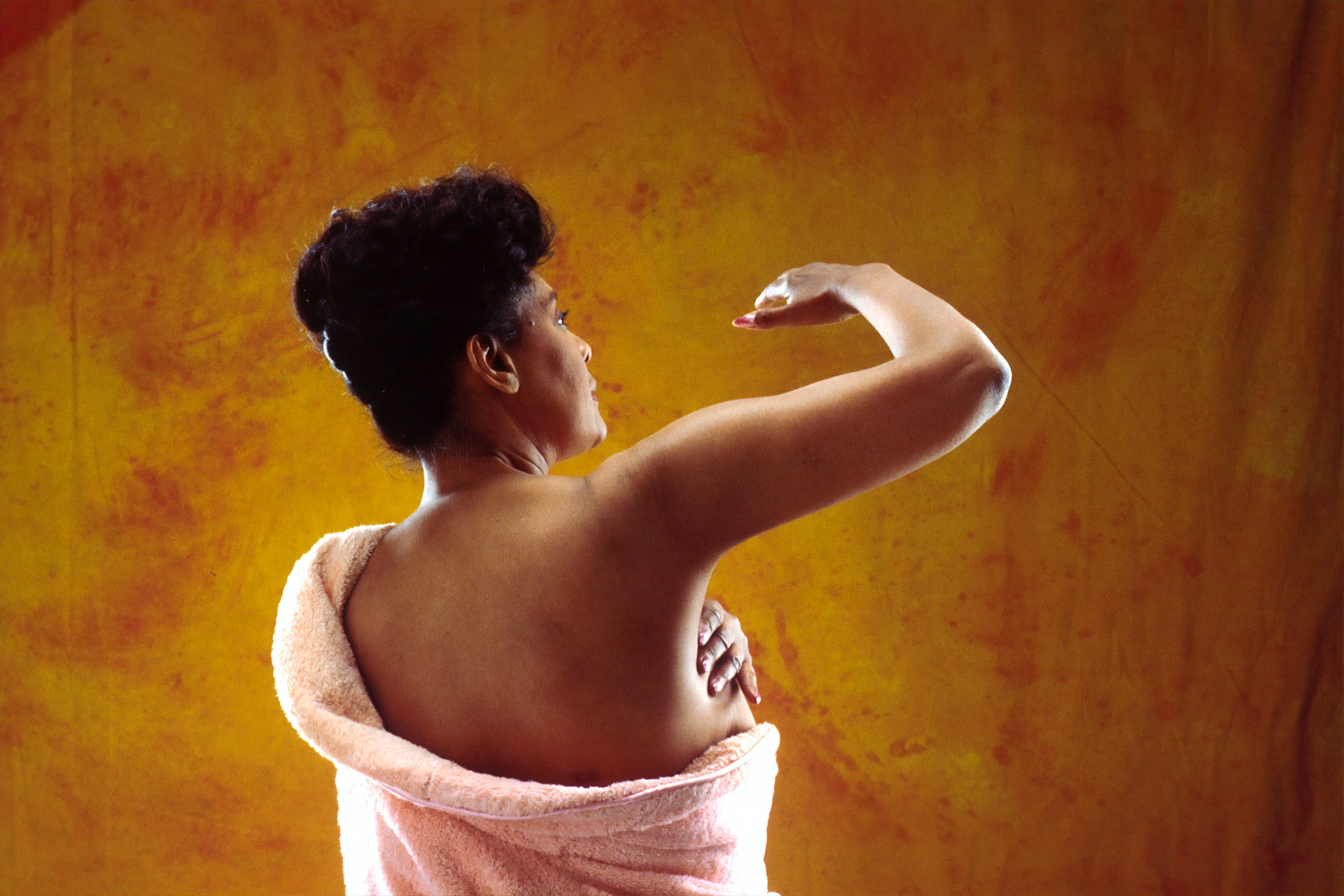 A rear view of an African American woman performing a breast self-examination